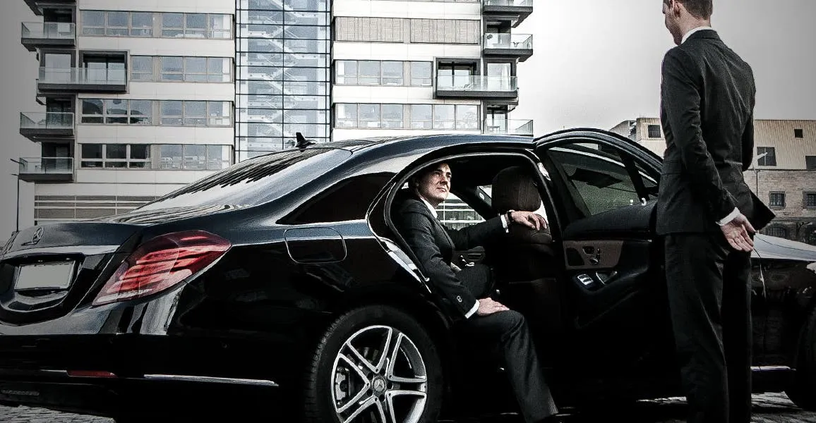Professional chauffeur helping a passenger into a luxury car